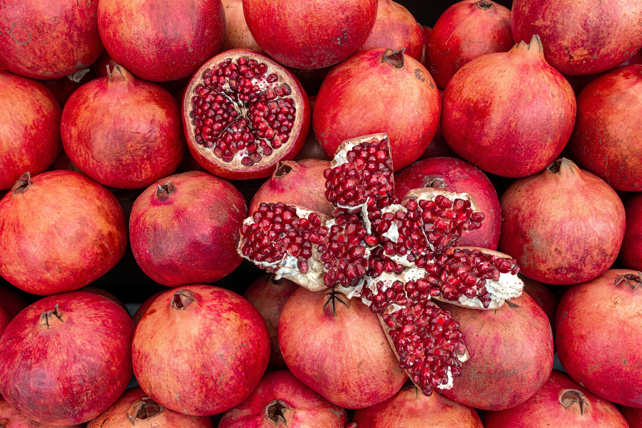 Viele rote Granatäpfel liegen dicht, einige sind geöffnet und zeigen Kerne.
