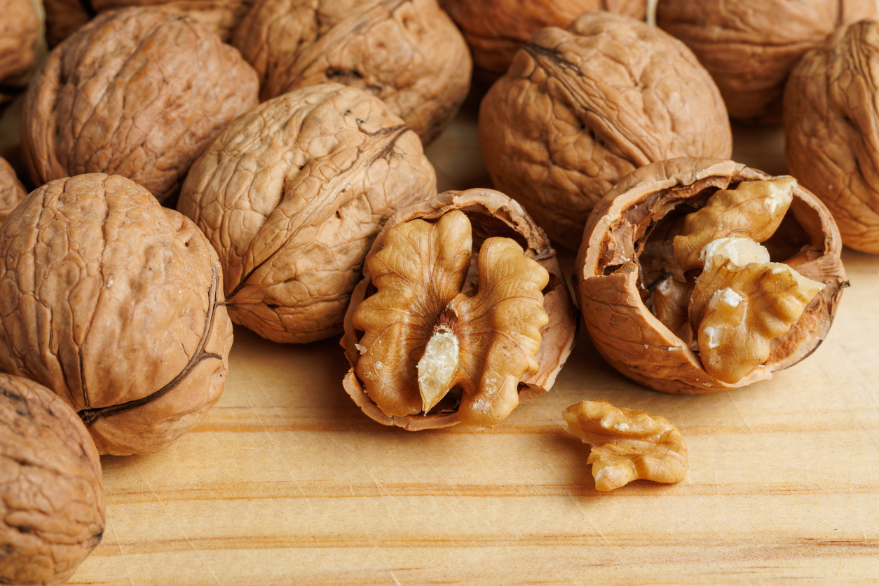 Nahaufnahme von ganzen und geknackten Walnüssen auf Holz.
