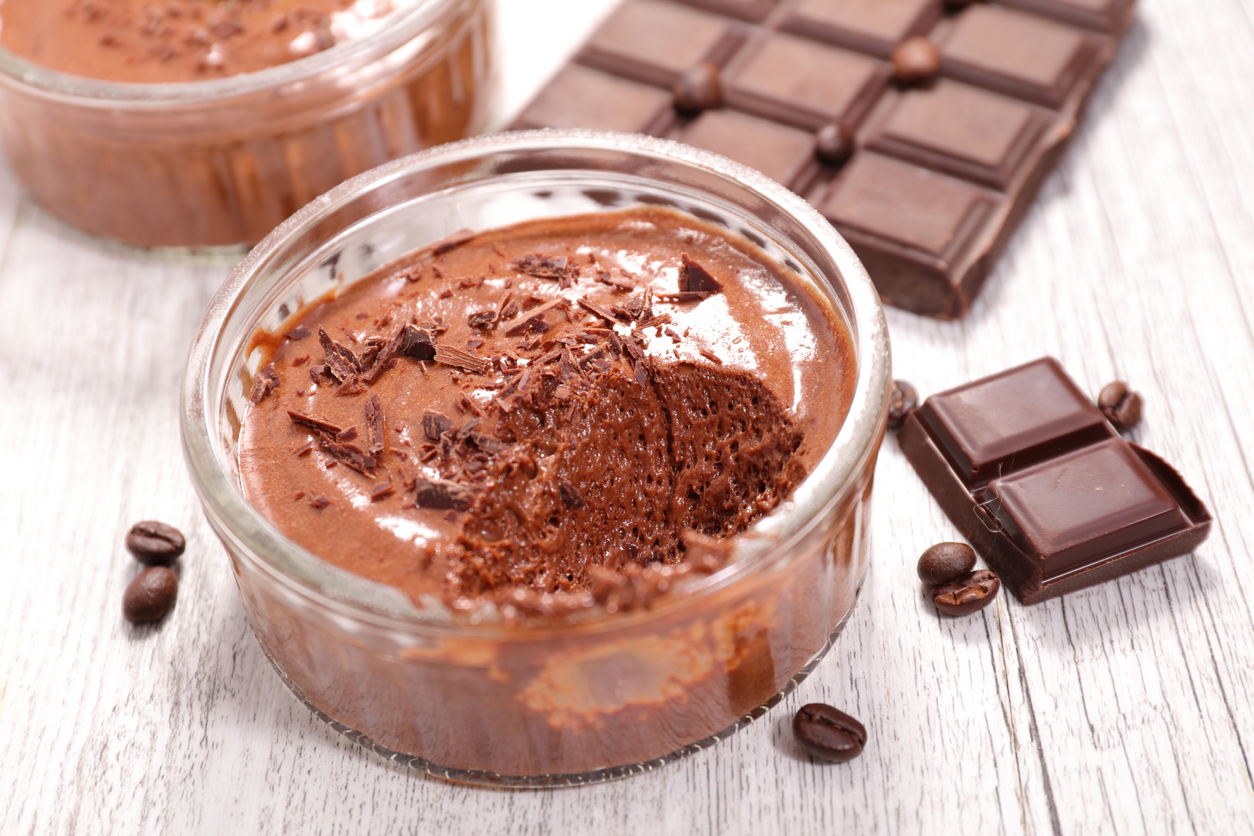 Glas mit Mousse steht neben Schokoladentafel und Kaffeebohnen.