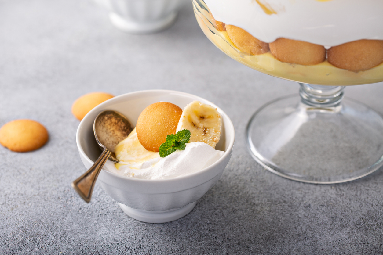 Eine Schale mit Bananenpudding mit Sahne und Keksschichten ist mit Banane, Keks und Minze garniert.