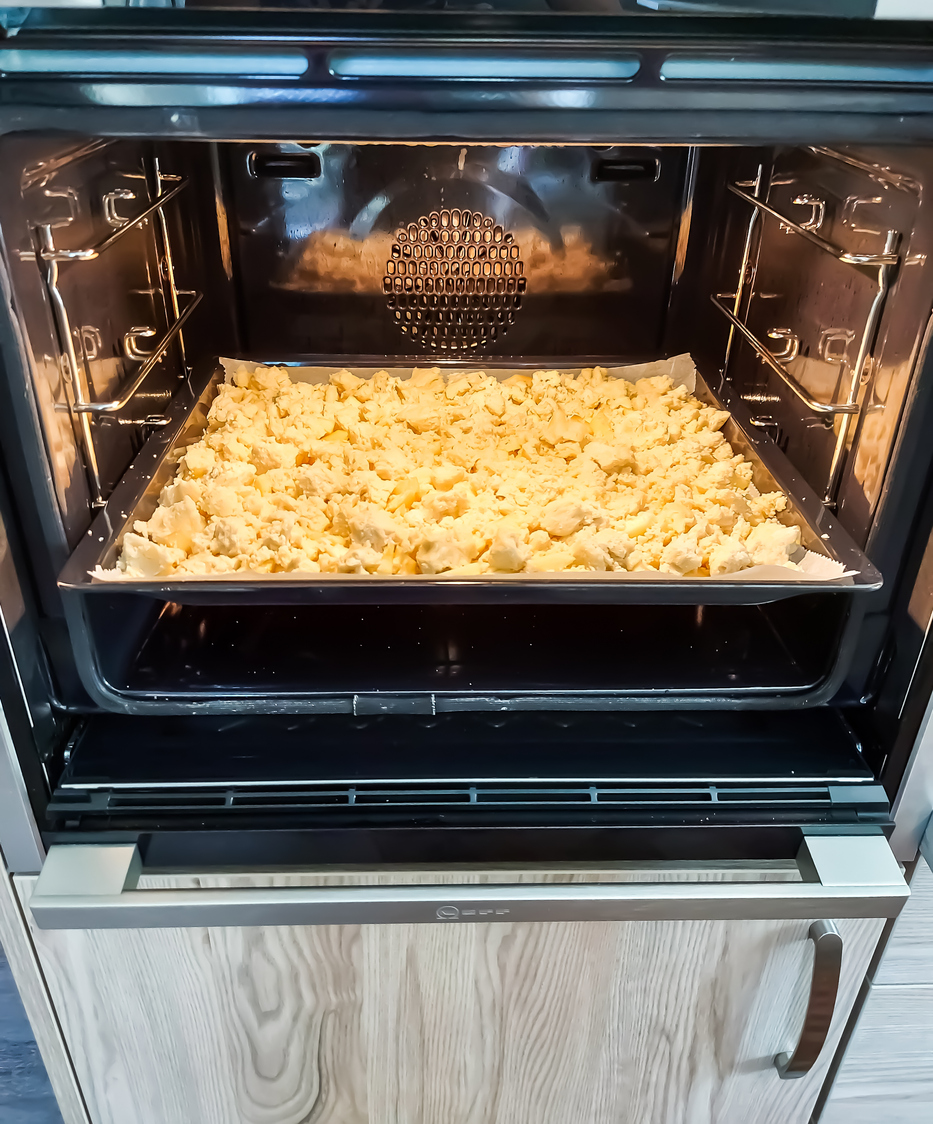 Ein Blech mit ungebackenem Apfelstreuselkuchen vom Blech steht im geöffneten Backofen.