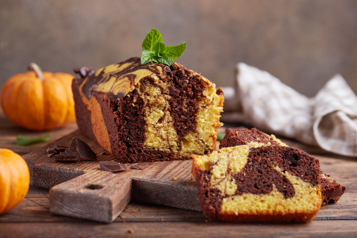 Auf einem Holzbrett steht ein angeschnittener Marmorkuchen mit heller und dunkler Marmorierung.