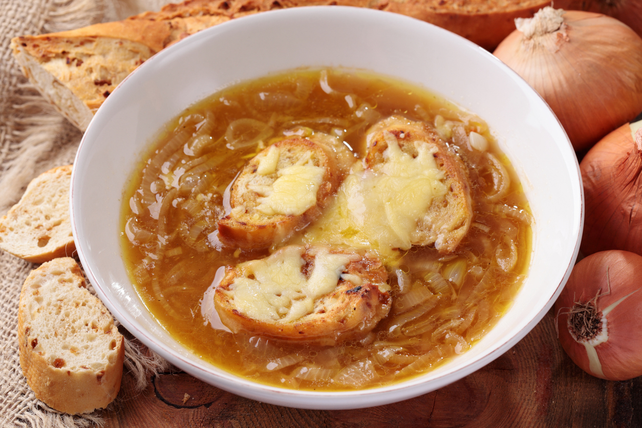 Französische Zwiebelsuppe in einer weißen Schüssel wird mit drei überbackenen Brotscheiben und geschmolzenem Käse serviert.