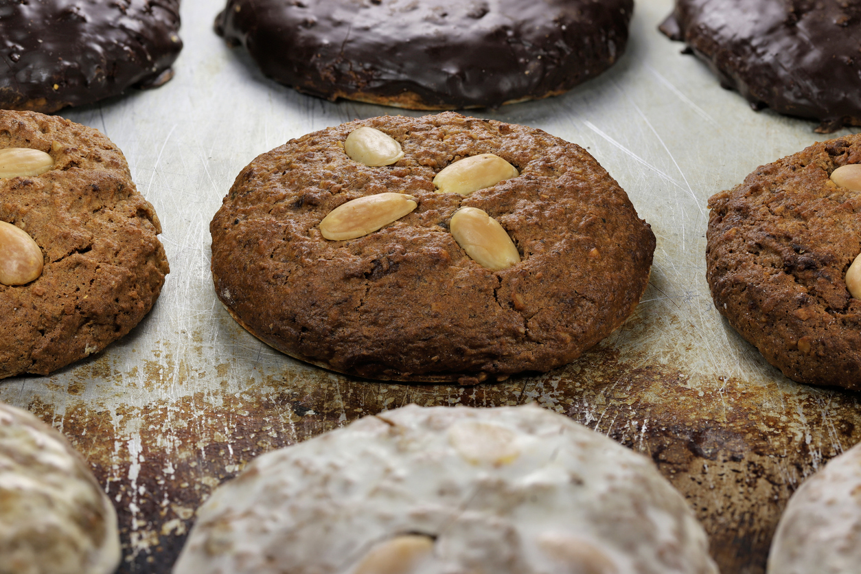 Mehrere Hausgemachte Lebkuchen mit Mandeln stehen mittig auf einem Blech, umgeben von glasierten und schokolierten Varianten.
