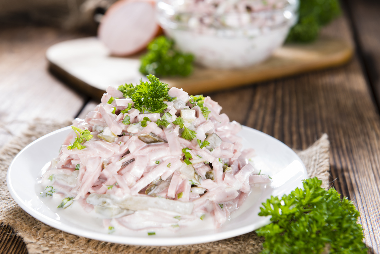 Ein Häufchen Fleischsalat mit Petersilie liegt auf einem weißen Teller, daneben frische Kräuter.