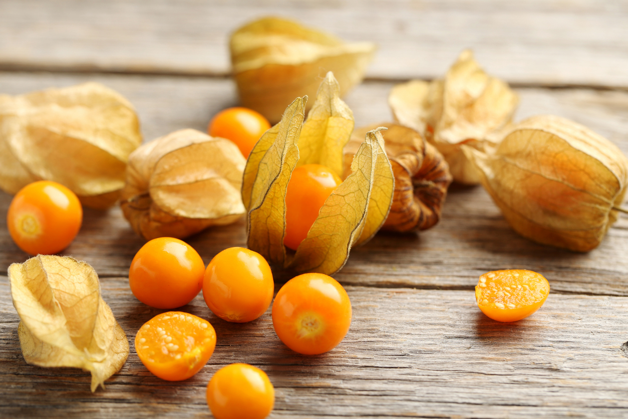 Mehrere gelb-orange Beeren und geöffnete Hüllen auf rustikalem Holz.