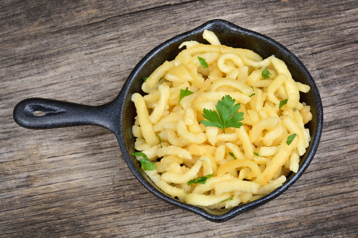 Kleine gusseiserne Pfanne mit selbstgemachten Spätzle und Petersilie auf rustikalem Holztisch.