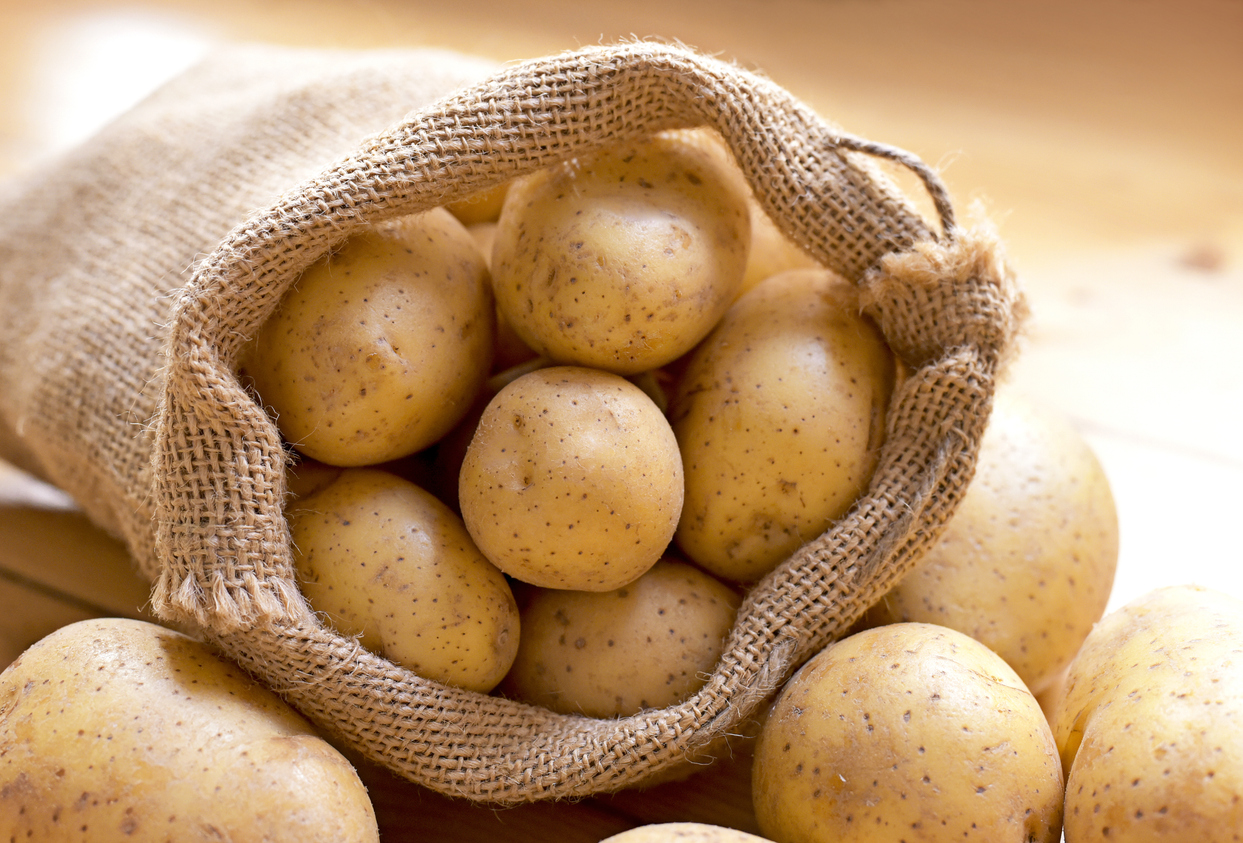Ein Jutesack ist mit Kartoffeln gefüllt und liegt auf einer hellen Fläche.
