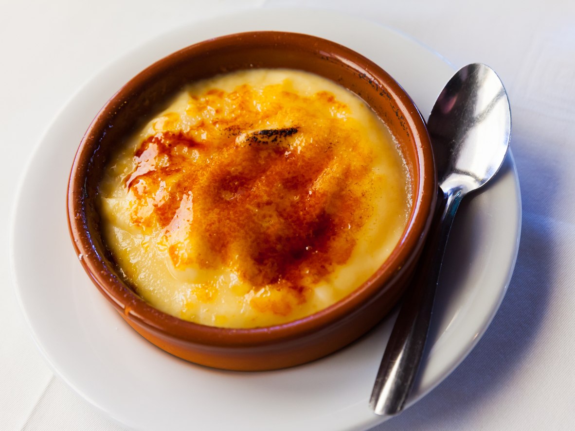 Crema Catalana in einer braunen Form steht auf einem Teller, daneben liegt ein Löffel.