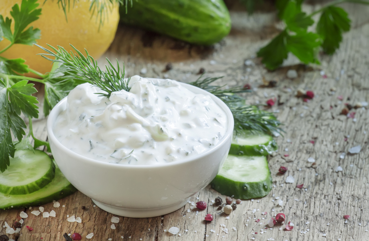 Ranch Dressing in einer weißen Schale mit Gurkenscheiben, Dill und Gewürzen auf Holzuntergrund.