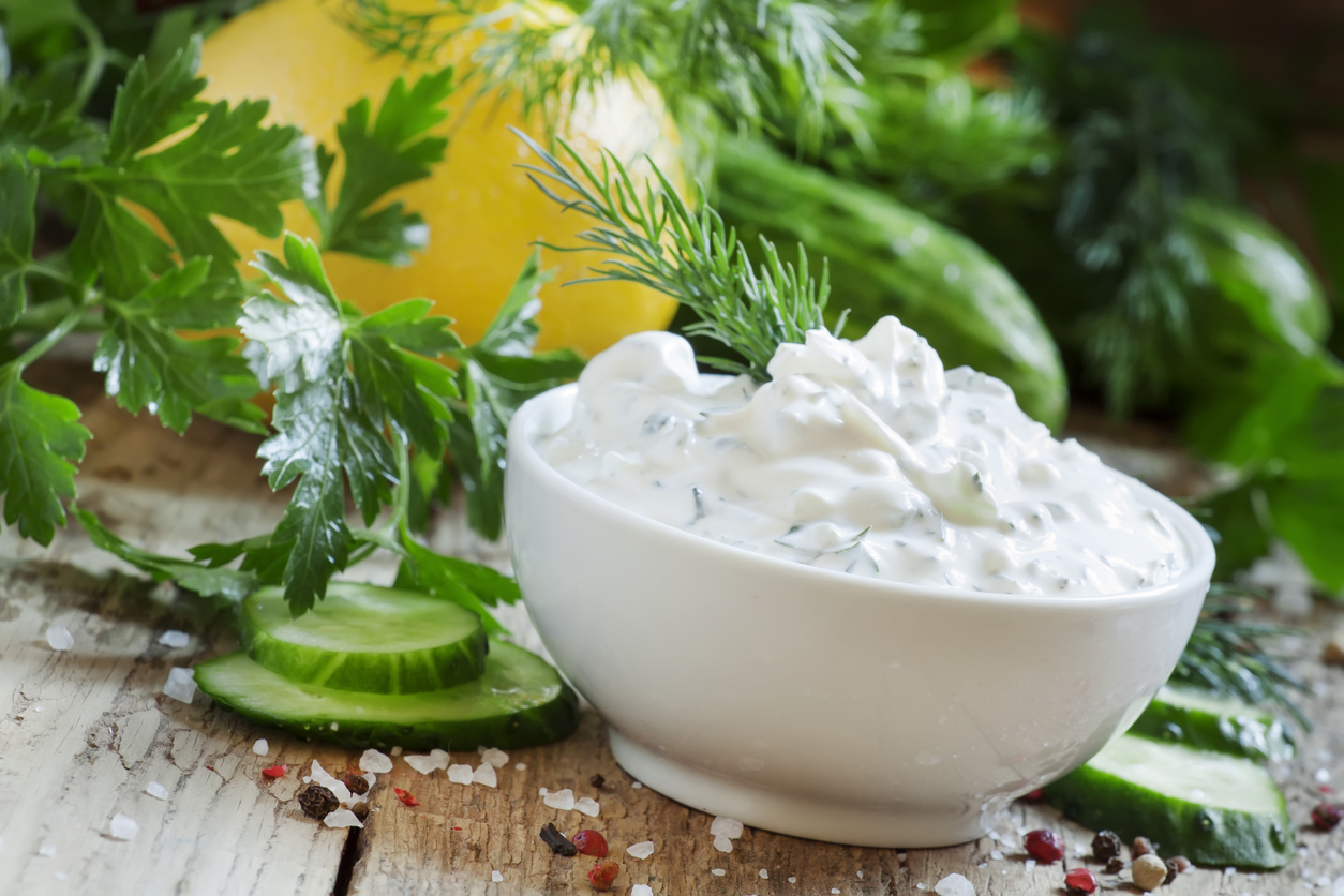 Schale mit cremigem Ranch Dressing, Dill, Gurkenscheiben und Kräutern auf rustikalem Holz.