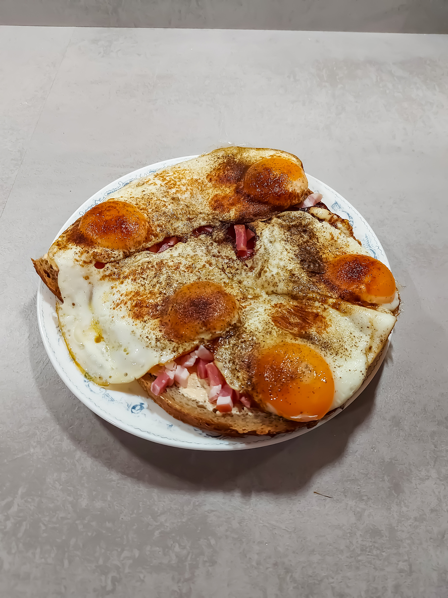 Ein Strammer Max mit Schinkenwürfeln und mehreren Spiegeleiern liegt auf einem Teller.