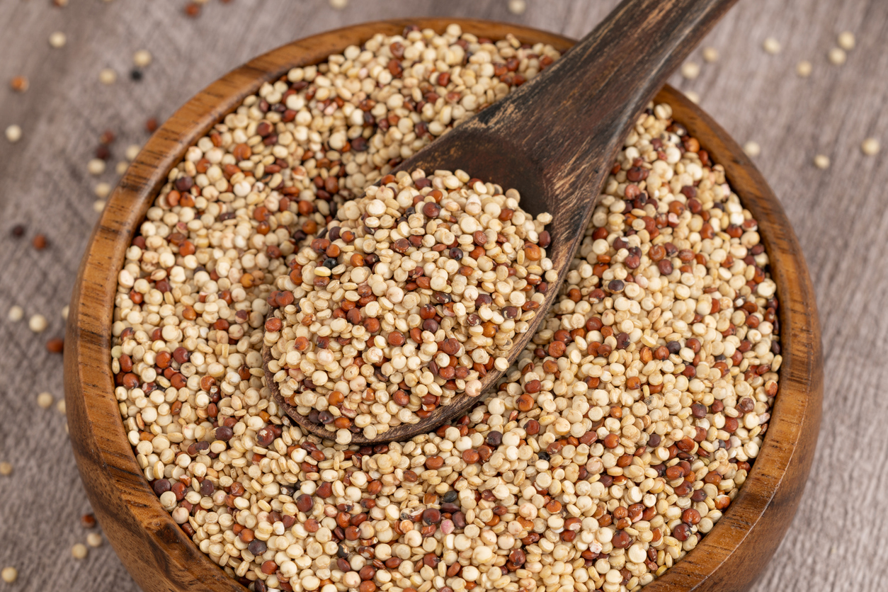 Quinoa liegt in einer Holzschale, ein Holzlöffel ist mit Körnern gefüllt.