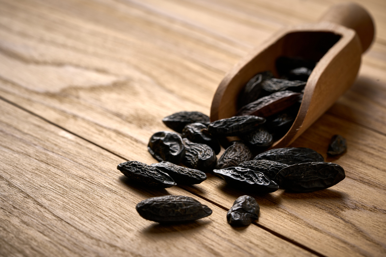 Schwarze Tonkabohnen liegen auf einem Holztisch neben einer umgekippten Holzschaufel.