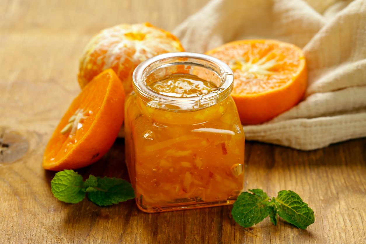 Offenes Glas Orangenkonfitüre auf Holztisch mit Orange, Orangenscheibe und Minzblättern.