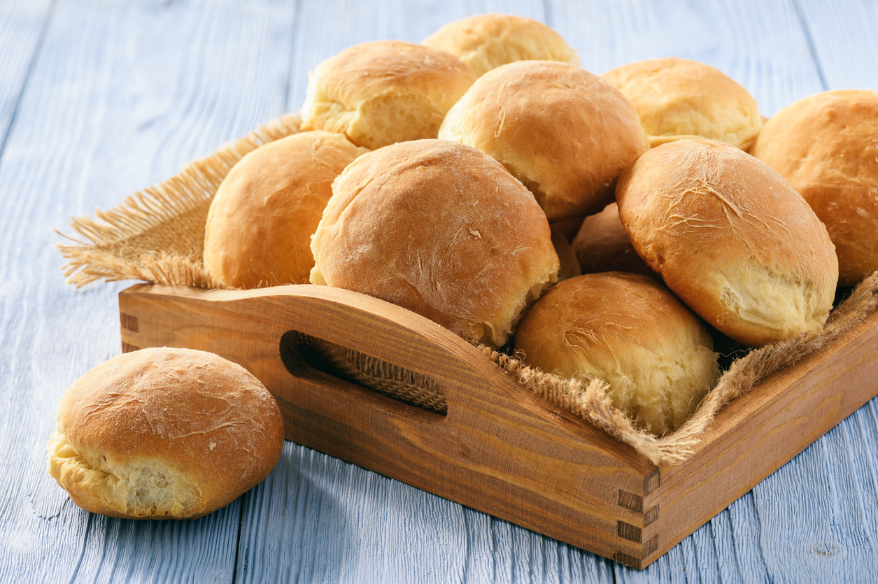 Kartoffelbrötchen sind in einem Holztablett gestapelt und ein einzelnes Brötchen liegt davor auf dem Tisch.