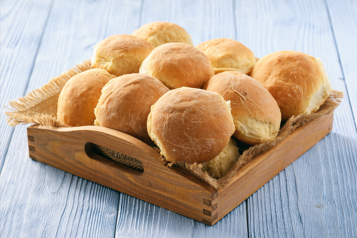 Kartoffelbrötchen liegen goldbraun gebacken in einem Holztablett auf hellblauem Holztisch.