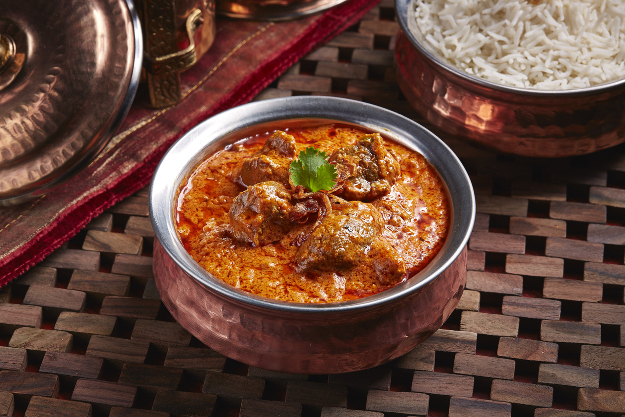 Rogan Josh Curry in einer Schale mit Reis im Hintergrund und frischem Koriander als Topping.