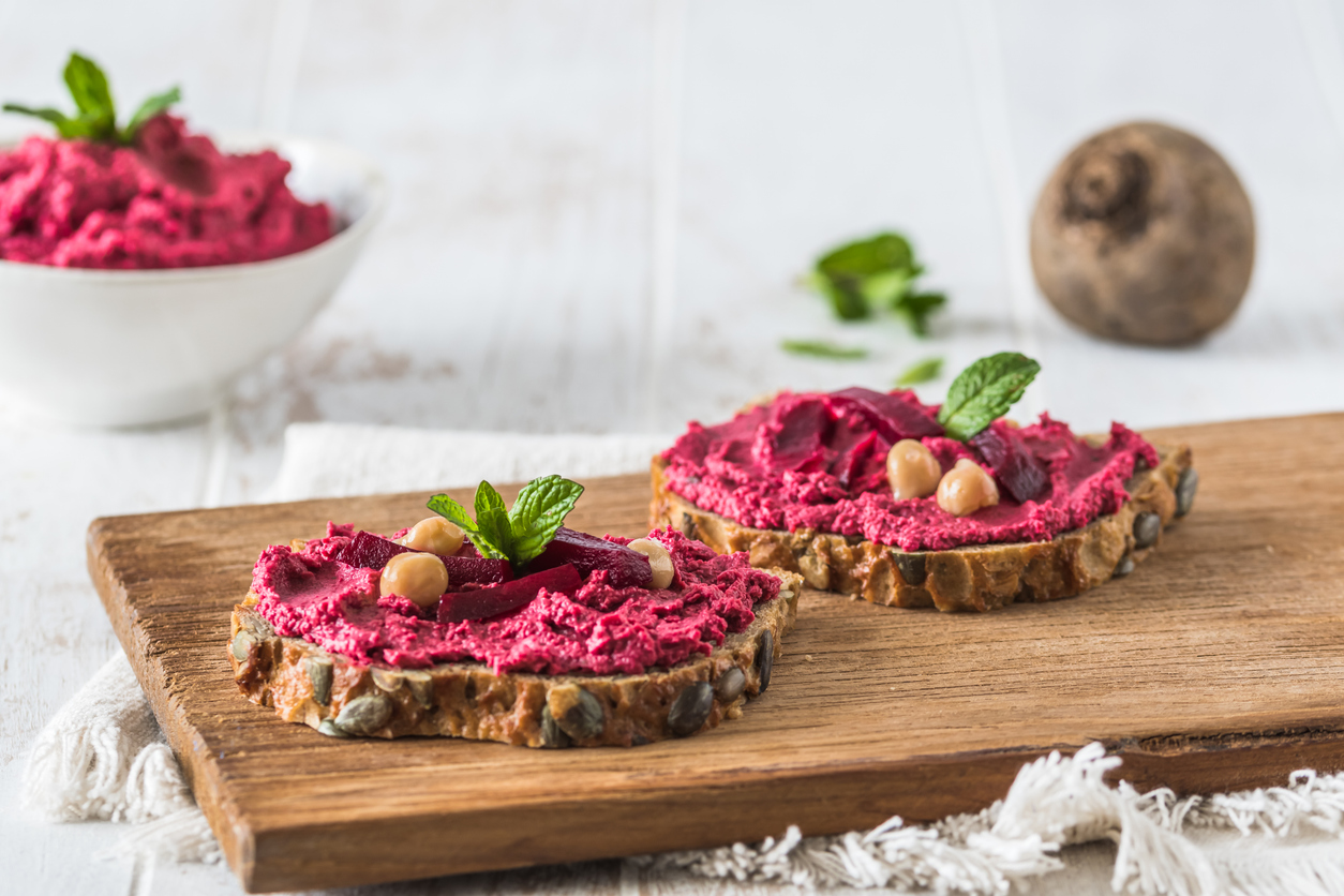 Ein belegtes Körnerbrot mit Rote Bete Hummus ist mit Rote Bete Stücken, Kichererbsen und Minze dekoriert.