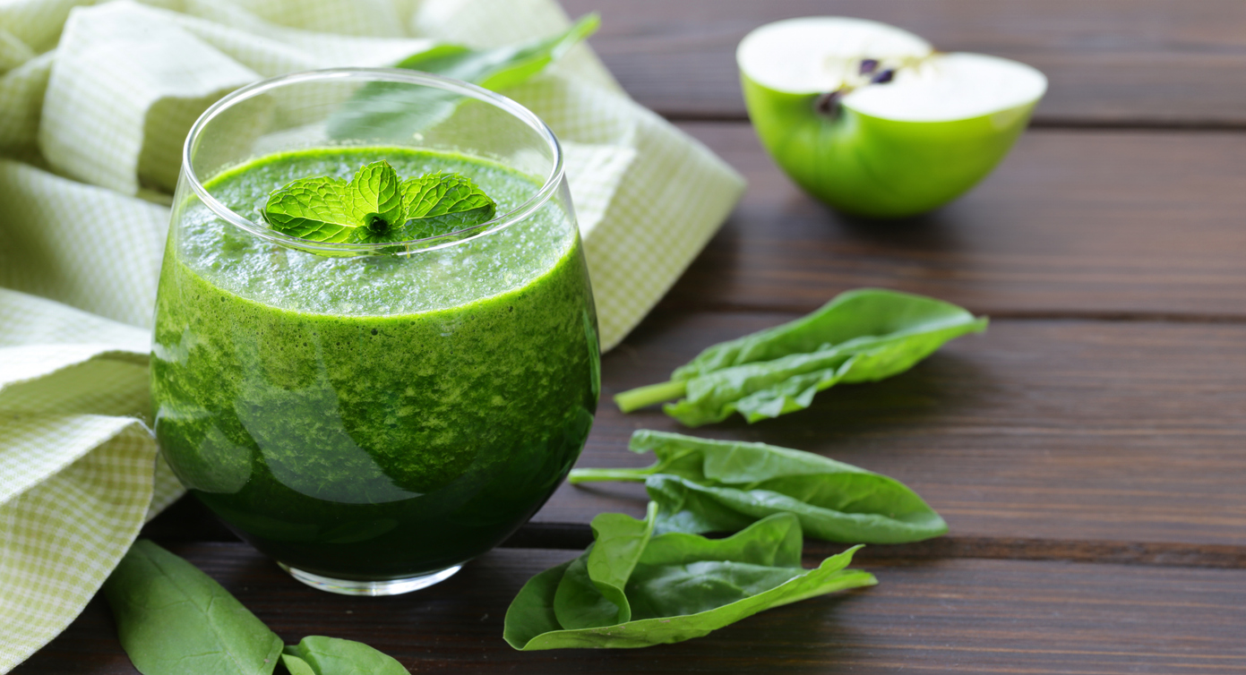 Ein cremiger Apfel-Spinat-Smoothie ist in einem runden Glas mit Minzblättern dekoriert.