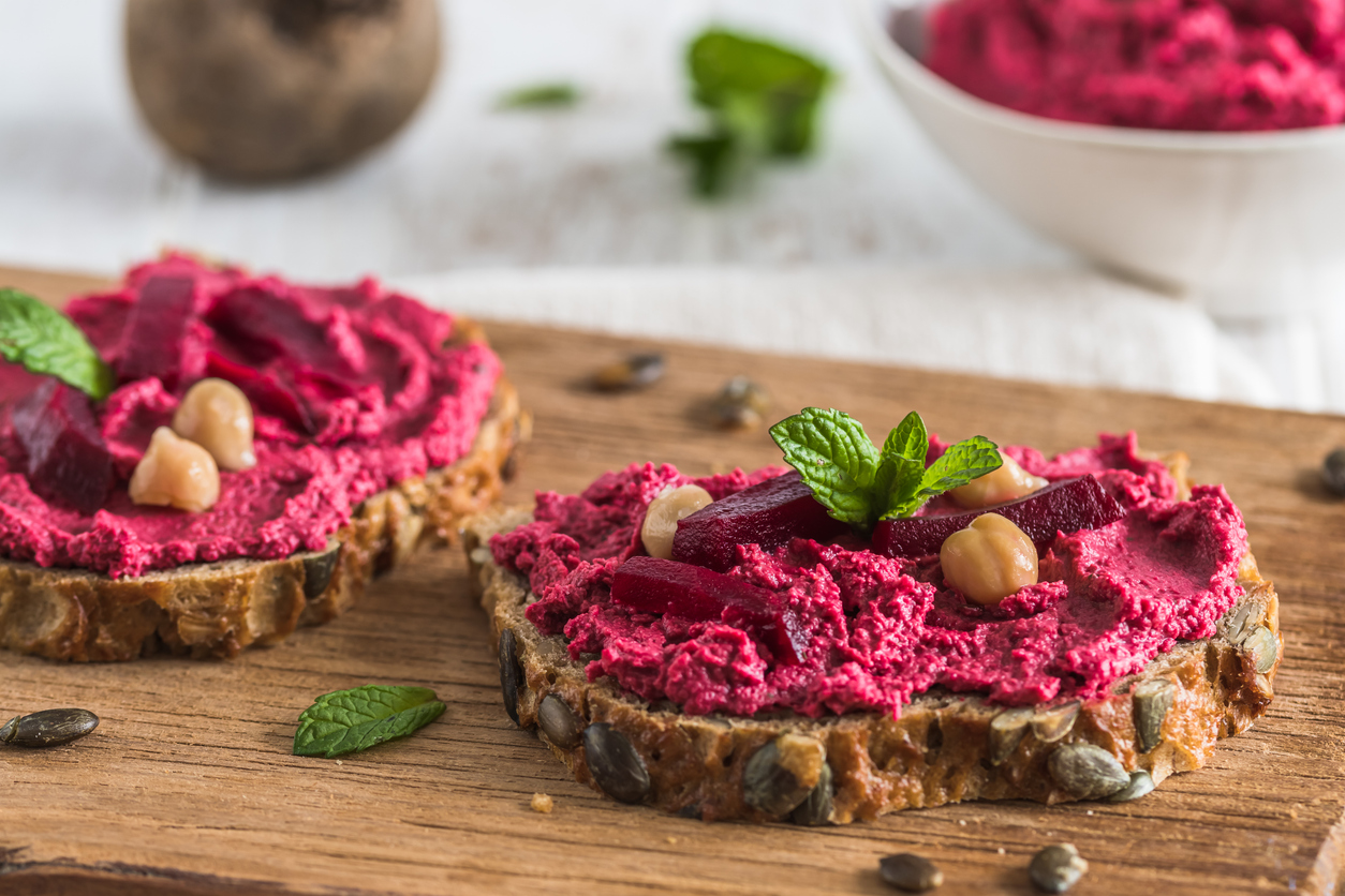 Zwei Brotscheiben sind mit Rote Bete Hummus bestrichen und mit Kichererbsen und Minze garniert.