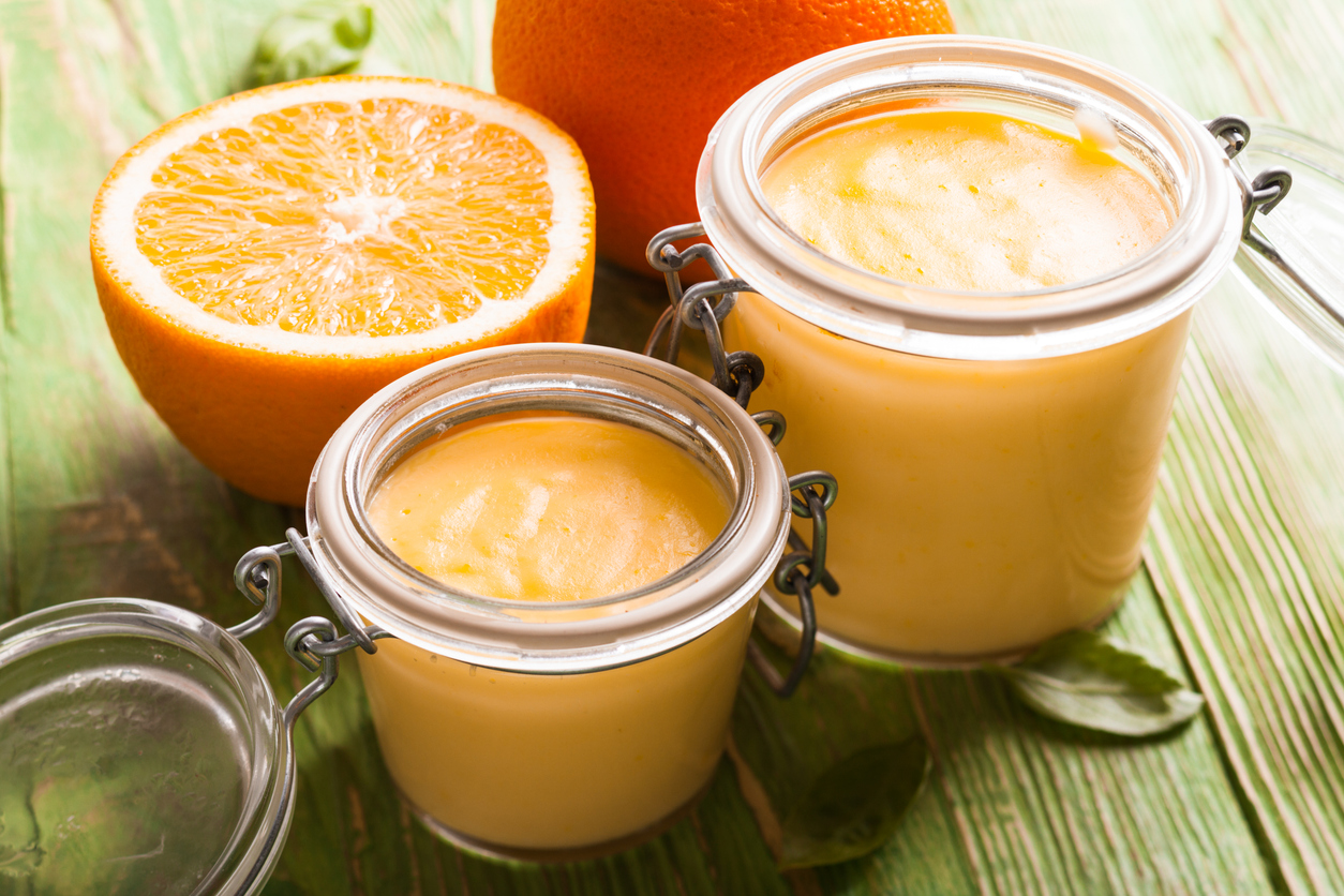 Zwei Bügelgläser mit Orangenquark stehen neben einer halbierten Orange auf einem Holzuntergrund.