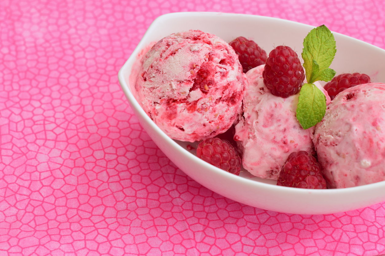 Kugeln von Himbeereis liegen in einer weißen Schale auf einem pink gemusterten Hintergrund.