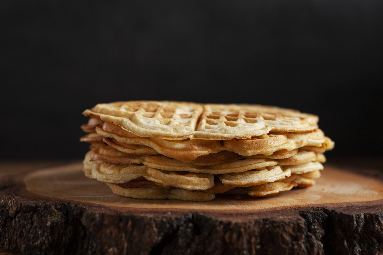 Fünf frisch gebackene, herzförmige Waffeln liegen übereinander gestapelt auf einer dunklen Holzoberfläche.