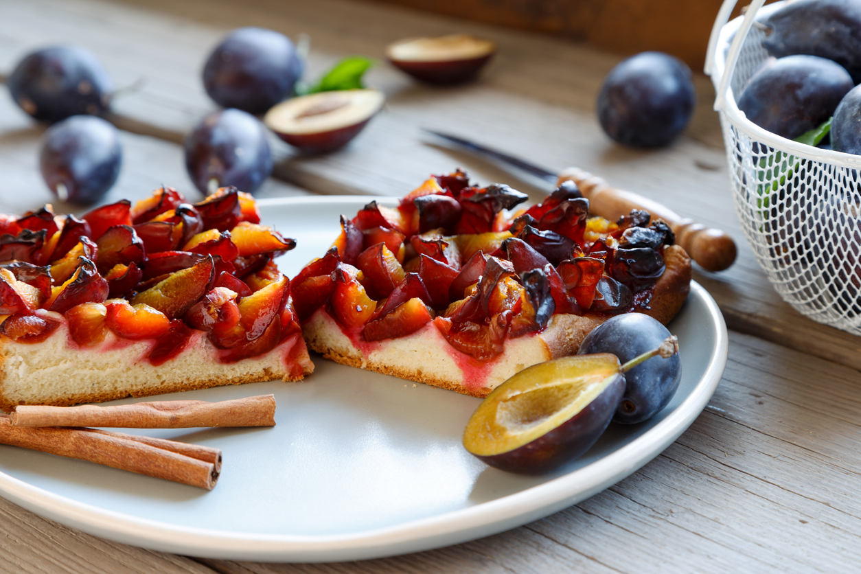 Zwei Stück Pflaumenhefekuchen liegen auf einem Teller, umgeben von frischen Pflaumen.