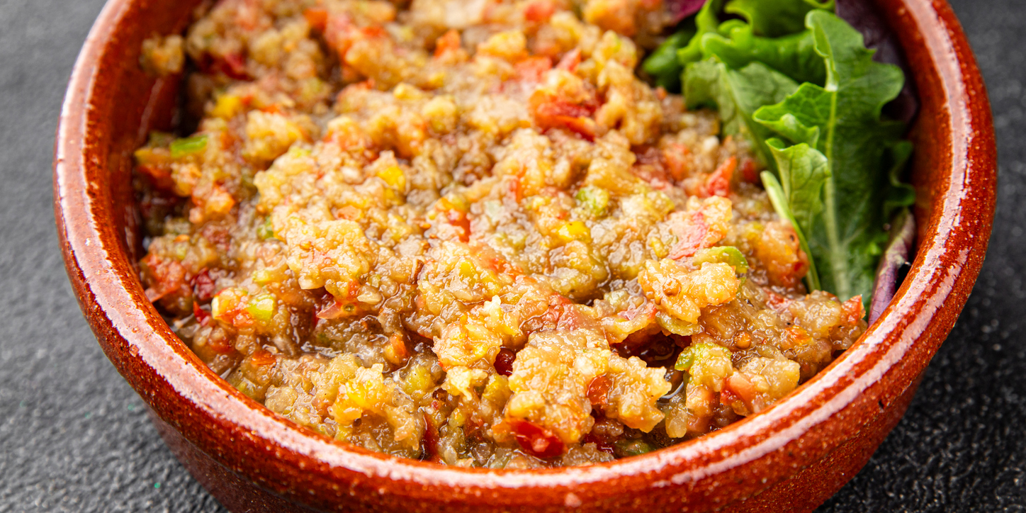 Ein Auberginen Dip füllt eine braune Schüssel und liegt neben frischen Salatblättern.