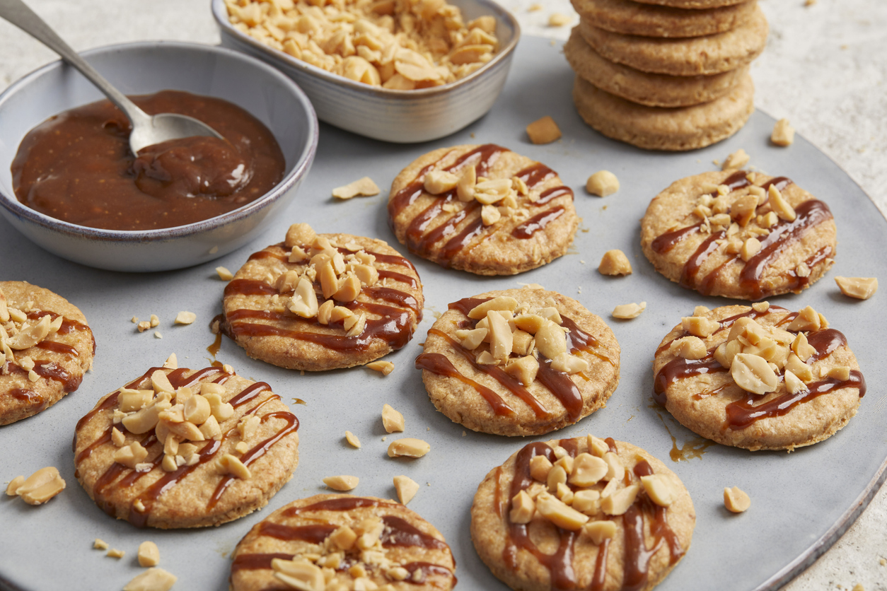 Mehrere goldbraune Haferkekse mit Kokos, die mit dunklen Karamellstreifen überzogen und auf einer grauen Platte angerichtet sind.